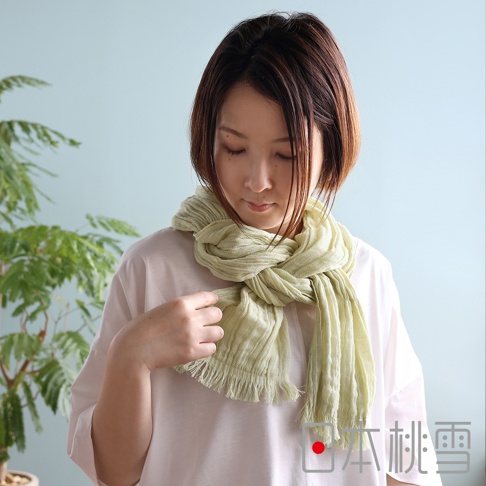 一位留著棕色短髮的女性低頭注視，脖子上圍著一條淺綠色的四季萬用抗UV純棉紗布圍巾，圍巾呈現皺褶紋理並帶有流蘇邊飾，搭配純白色上衣，畫面右下方印有日本桃雪品牌標誌。