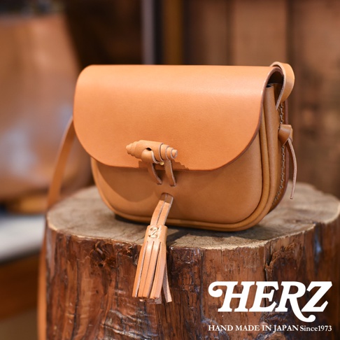 職人手作皮革流蘇側背包 CP-18，採用天然皮革製作，呈現溫潤的棕褐色調。包款設計簡約，附有獨特的皮革編織鎖扣及流蘇裝飾，展現精緻的手工質感。