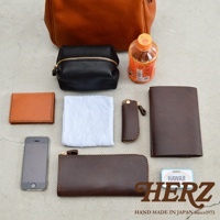 職人手作皮革Organ方形口金托特包 G-55，展示內容包含咖啡色皮革托特包、黑色皮革化妝包、棕色皮革名片夾、白色布巾、棕色皮革鑰匙包、棕色皮革長夾、手機及一瓶飲料。