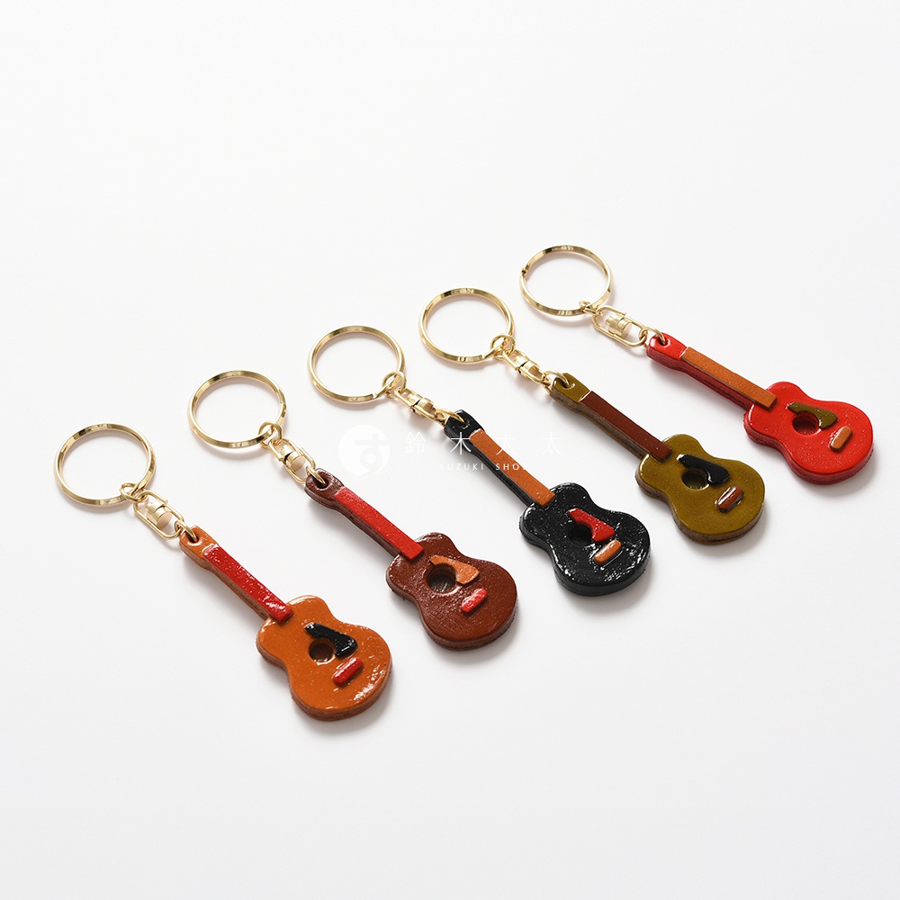 職人手作皮革吉他造型鑰匙圈，共有棕色、紅色、黑色、黃褐色五種顏色，以皮革材質製作，每個鑰匙圈皆附有金色鑰匙環。