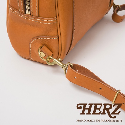 職人手作皮革軟皮商務後背包 R-28，特寫展示其棕褐色皮革材質、黃銅金屬扣環與細膩車縫線，以及可拆卸的皮革背帶。