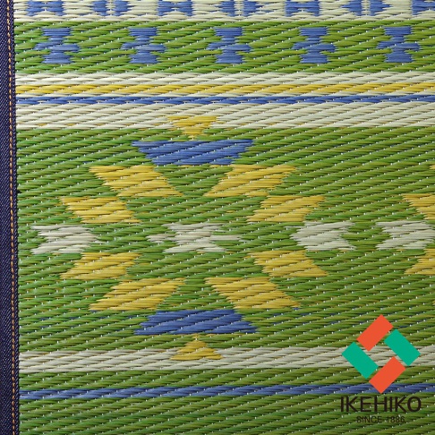 綠色藺草編織的瑜珈墊，帶有黃色、藍色和白色交錯的幾何圖案。