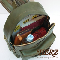 橄欖綠皮革後背包，內部裝有筆記本、錢包、紅色皮夾和一瓶水。