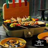 淺綠色迷你烤盤上烤著烤肉串，有雞肉、青椒、紅椒、櫛瓜和花椰菜，旁邊有木製竹籤架，架上插著彩色竹籤。右下角為黃色盤子，盤中盛有淡菜。