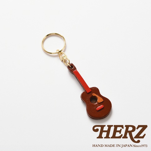 職人手作皮革吉他造型鑰匙圈，主體為深棕色皮革，琴頸部分為紅色皮革，搭配金色掛環，精緻小巧。