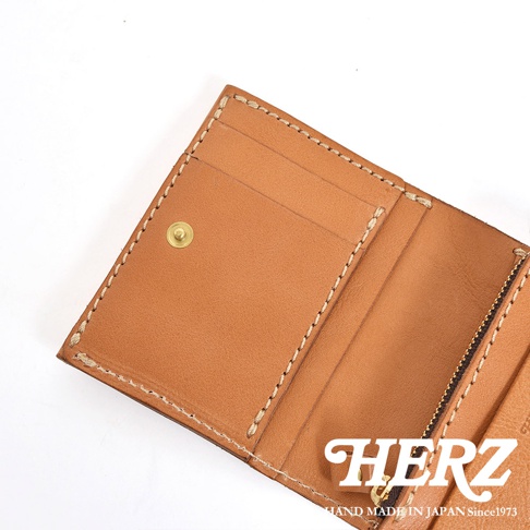 這是一款日本HERZ手工製作的皮革雙折短夾，呈現淺棕色原色皮革質感，內部設有直式卡片夾層、黃銅色按扣以及配備防落側翼的L型拉鍊零錢袋，整體縫線細膩，展現日式職人工藝風格。