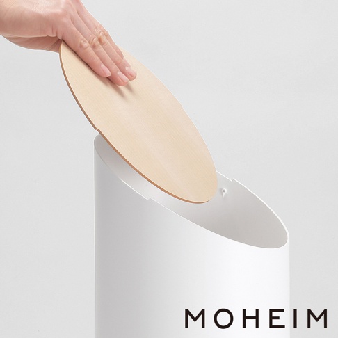 一只手正將一個圓形的胡桃木蓋子放在一個白色的垃圾桶上。