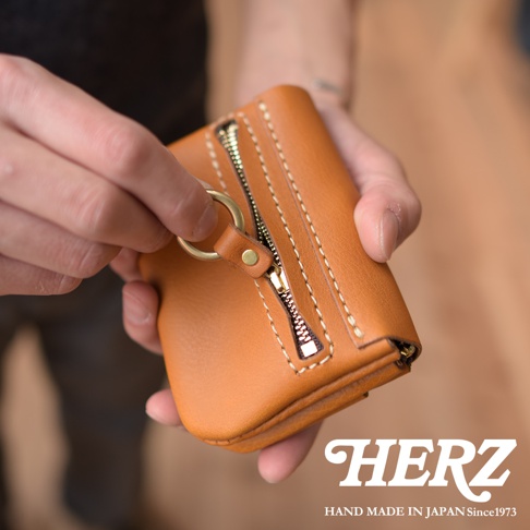 職人手作皮革旅行用雙層錢包，以天然棕色皮革製成，配有黃銅色拉鍊與掛環，縫線清晰，質感細膩。