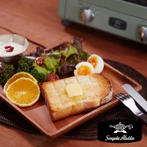 淺綠色復古多用途烤箱，特寫盤中早餐：抹有奶油的格子吐司、水煮蛋、沙拉、水煮花椰菜、柳橙片和優格。