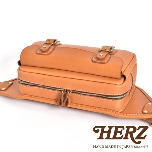 職人手作皮革騎士隨身斜背包，以棕色皮革製成，配有雙拉鍊開口、兩個搭扣裝飾，風格簡約實用。