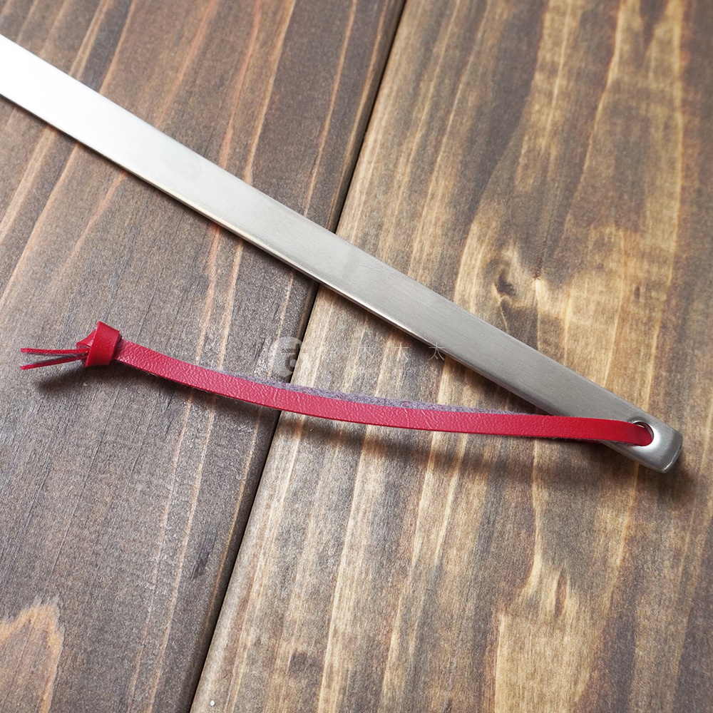 不鏽鋼萬用撈油勺，勺柄為銀色不鏽鋼材質，末端繫有紅色皮革掛繩，掛繩內嵌灰色織物。