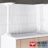 白色伸縮防傾桿，由塑膠材質製成，頂端有固定板，底部有可調節的底座，固定在白色櫃子上方，與有垂直線條紋的壁紙形成對比。