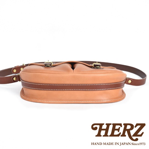 職人手作皮革傳統釣魚包，淺棕色皮革主體，深棕色皮革滾邊，縫線細緻，配有黃銅色金屬扣環與皮革背帶。