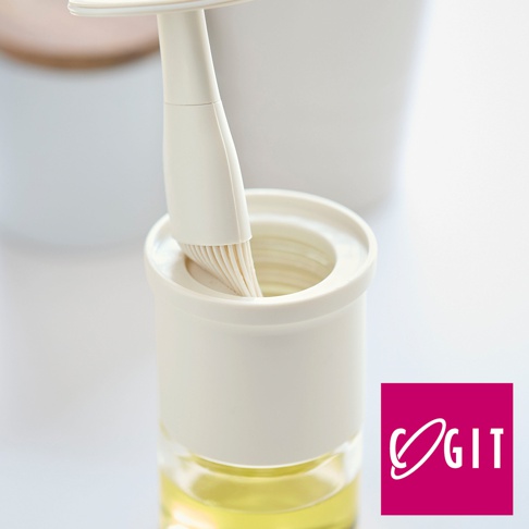 一個奶油色矽膠油刷，其刷毛插入一個奶油色帶有螺旋蓋的玻璃罐中，罐中裝有淺黃色液體。