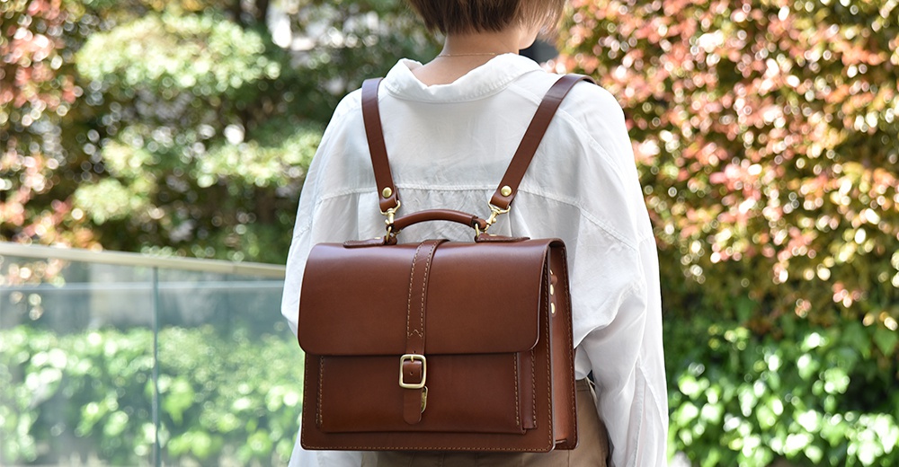 棕色皮革三用單扣商務後背包，配有金色扣環和可調節肩帶，可肩背或後背。