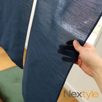 深藍色手作門簾，細緻織紋，半透明材質，邊緣縫線清晰，展示於窗邊，搭配木質地板和綠色坐墊。