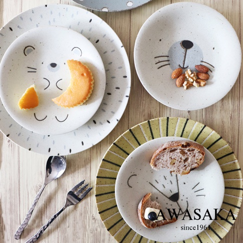 Mogu Mogu 萌萌動物餐盤2入組(獅子)由兩個陶瓷餐盤組成，一個上面印有淺灰色獅子臉，搭配橘色餅乾和橘色水果塊；另一個是較大的淺灰色餐盤，點綴著黑色不規則斑點，上面放著另一個印有獅子臉的白色餐盤，盤上有堅果和餅乾。