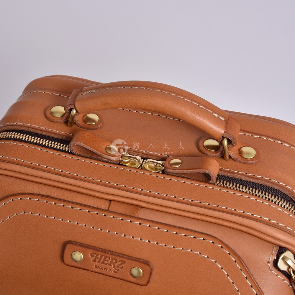 職人手作皮革兩用商務後背包 R-33，特寫鏡頭展示了焦糖色皮革的細緻紋理、手工縫線、黃銅拉鍊及品牌標誌。