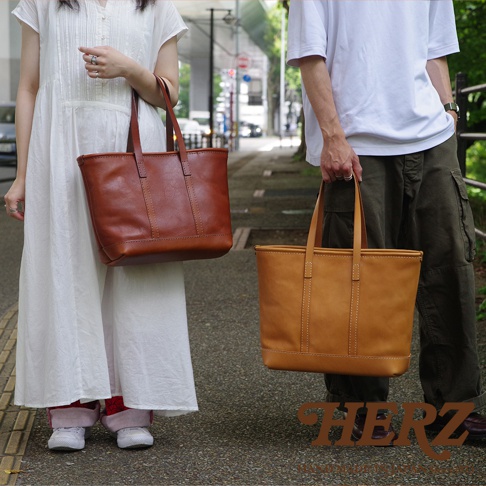 兩款職人手作皮革經典托特包，左為棕褐色，右為淺棕色，皆為簡約大方的托特包款，搭配雙提把設計，展現皮革的自然紋理與質感。