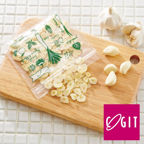 透明密封保鮮袋裝有切片蒜頭，袋上印有綠色蔥、蒜、九層塔等辛香料圖案。旁邊的木質砧板上散落著幾顆新鮮蒜頭。