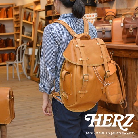 職人手作皮革經典雙扣後背包 R-152，採用棕褐色皮革製成，設計有雙扣翻蓋、側邊口袋及可調式肩帶，風格復古實用。