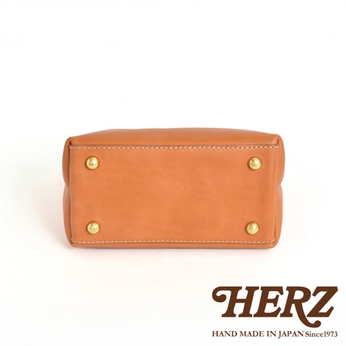 職人手作皮革迷你托特包 T-11，展示為經典的棕褐色皮革材質，包身底部設有四顆金色金屬腳釘，縫線整齊，展現簡約俐落的設計。