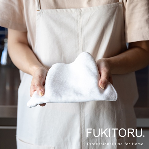 雙手拿著一塊白色超細纖維擦拭布，布料柔軟，表面有細密的紋理，呈現立體皺褶。