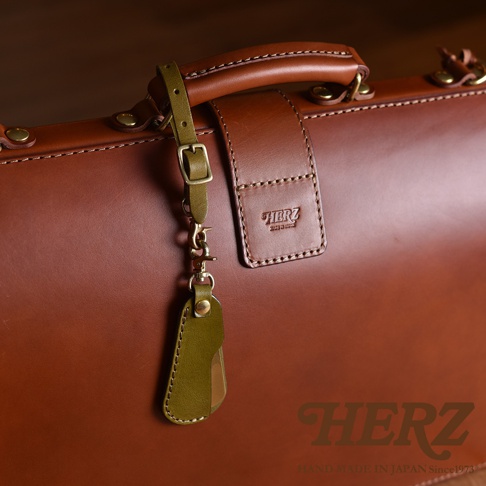 職人手作皮革隨身金屬鞋拔，搭配橄欖綠皮革吊飾與黃銅扣環，展現精緻工藝。