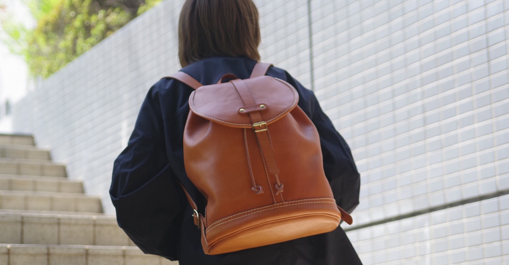 駝色皮革單扣束口後背包，配有可調式肩帶及束繩開口，適合日常攜帶。