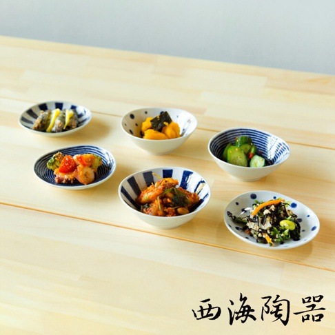 六個波佐見燒醬料碟，其中三個為藍色條紋，三個為藍色圓點，盛有各式日式小菜，如章魚、漬物、沙拉等，擺放在淺木色桌面上。