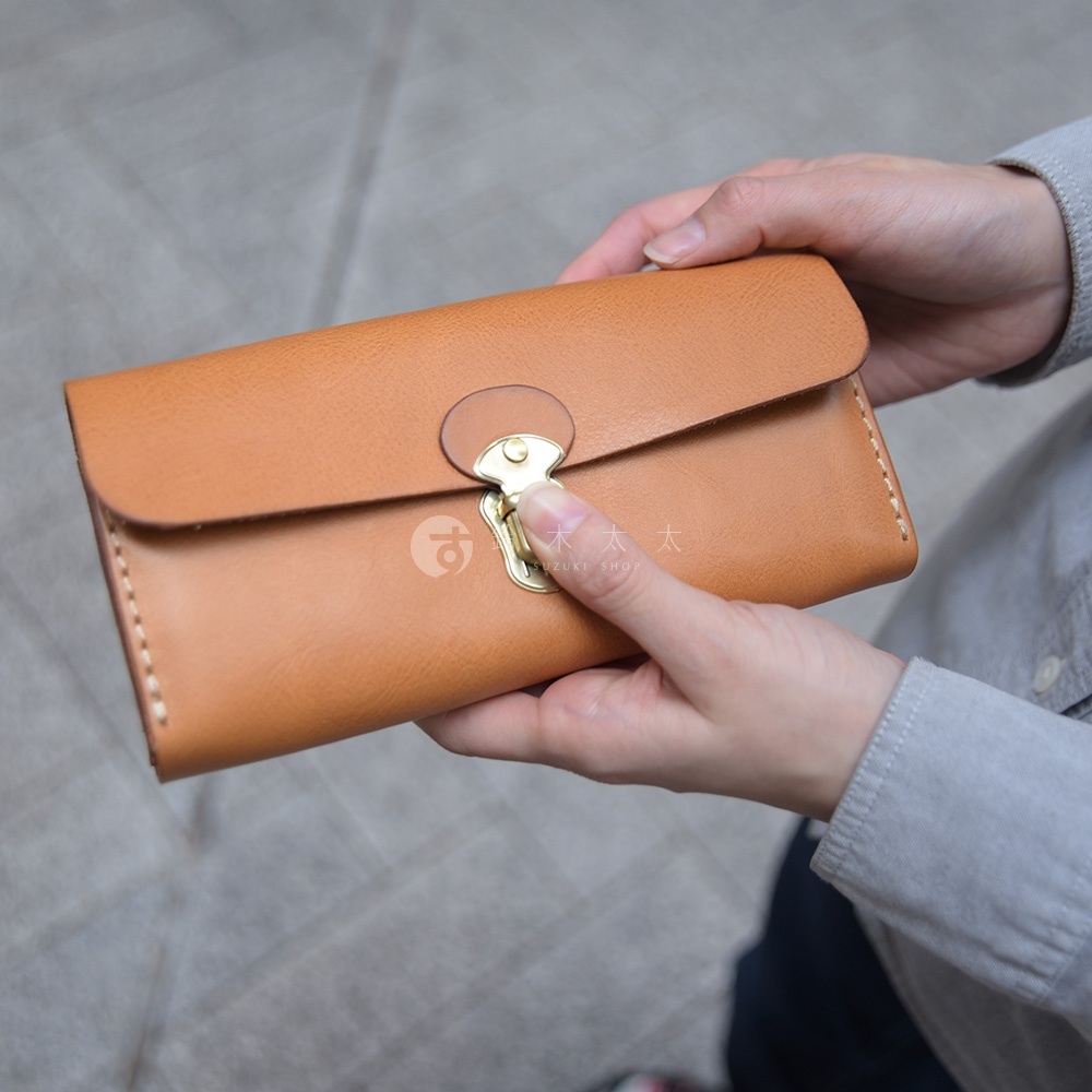 職人手作皮革長夾，呈現自然原色，配備金色金屬鎖釦及精緻縫線，展現簡約而經典的設計風格，適合日常攜帶多樣卡片與物品。