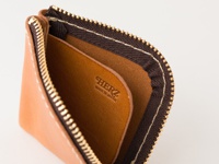 職人手作皮革分隔收納零錢包，淺棕色皮革，內有深棕色皮革隔層，金色拉鍊，白色縫線，印有「HERZ MADE IN JAPAN」字樣。
