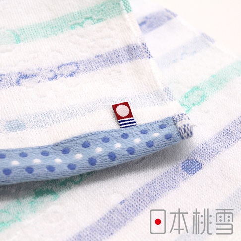 今治小花毛巾，白色毛巾上飾有藍綠色條紋，一條淺藍色滾邊點綴著藍色及白色圓點。毛巾邊緣有一個紅色標籤，上面印有白色圓形圖案和藍色條紋。