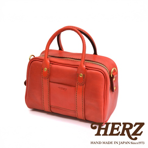 HERZ 品牌手工製作的橘紅色皮革迷你波士頓包，採用車縫線裝飾，配有手提帶和可拆卸肩帶。