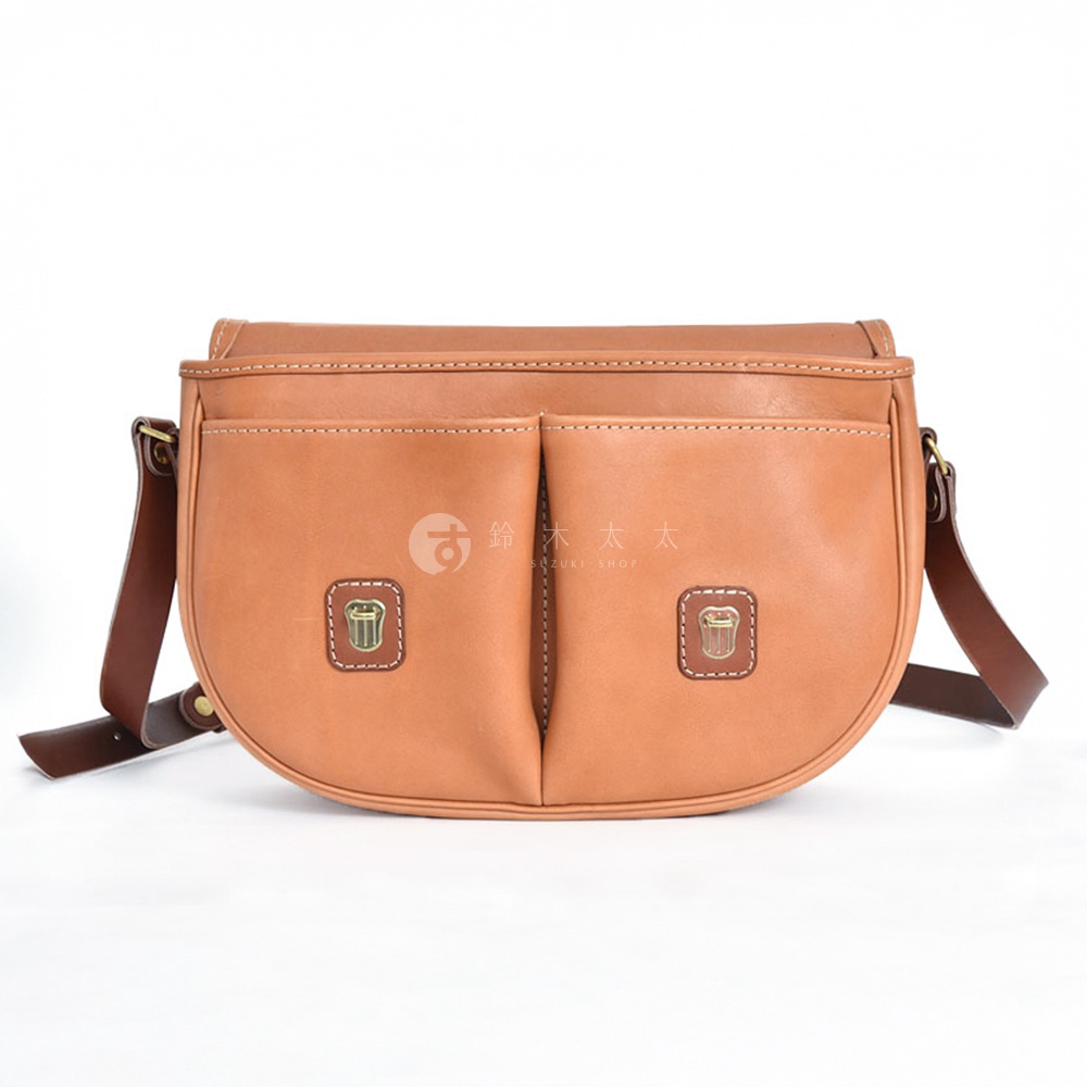 職人手作皮革傳統釣魚包，淺棕色，設有兩個前袋，每個袋上飾有小巧的徽章，搭配深棕色皮革肩帶。