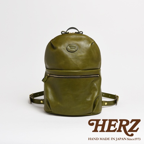 橄欖綠皮革大開口圓角後背包，有兩個外部拉鍊口袋，頂部有提把和品牌標誌，背帶為皮革材質。