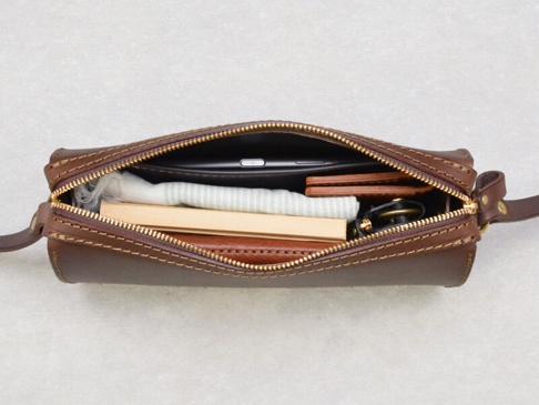 職人手作皮革Organ極簡風拉鍊單肩包，深棕色皮革，拉鍊開啟，內部可見手機、薄型錢包、鑰匙圈及條紋布料。
