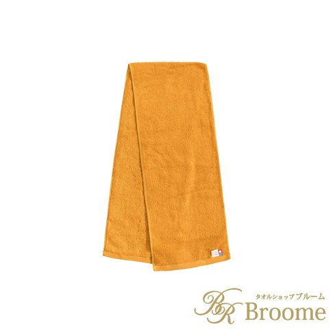 一條橘黃色的今治純棉掛脖毛巾，材質柔軟，有兩個標籤，其中一個標有「Broome」字樣。