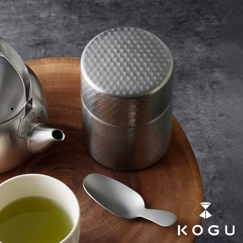 日製18-8不鏽鋼錘目紋茶葉罐，附有相同材質的茶匙，罐身與頂蓋皆有細膩的錘目紋路，呈現銀色金屬光澤。