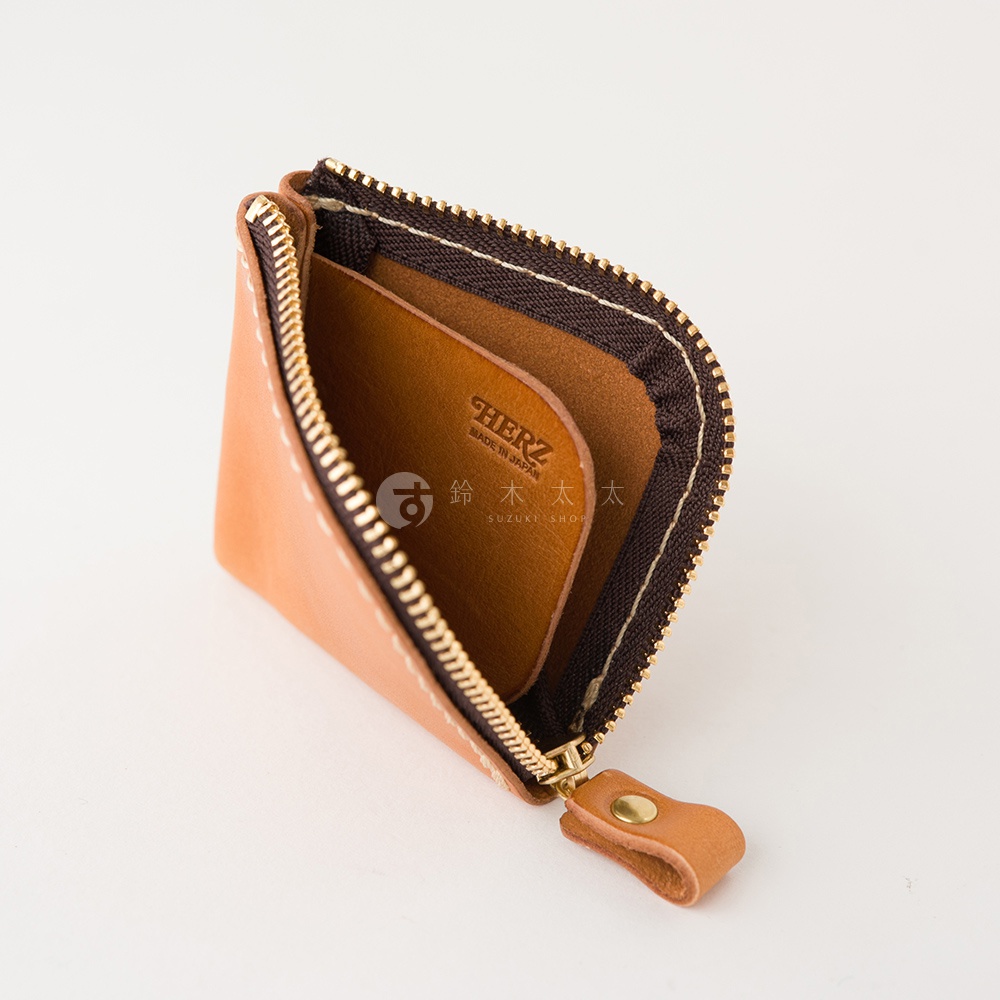 一個淺棕色的日本HERZ品牌職人手作皮革零錢包，採用耐用的Stare皮革製成，表面呈現自然的皮革紋理。包身設計精巧，搭配金色拉鍊與皮革拉環，開口處可見內部空間以及HERZ MADE IN JAPAN的品牌鋼印，整體展現簡約實用的日系職人風格。