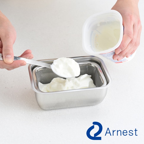 Arnest 不鏽鋼多功能濾網保鮮盒，使用湯匙舀取優格放入濾網中，旁邊為裝有優格的白色容器。