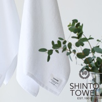 YUKINE 雪中漫步有機棉蓬厚迷你浴巾，白色，材質為 100% 棉。浴巾蓬鬆柔軟，邊緣縫有品牌標籤，一旁擺放著綠葉裝飾，整體呈現簡約純淨的風格。