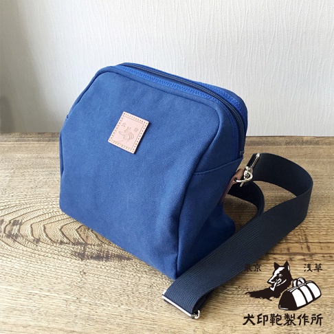 石洗帆布散步包，藍色，附有皮革標籤和黑色斜背包帶。