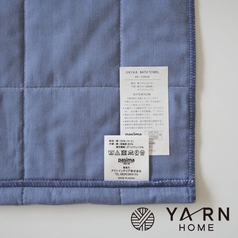 藍色格紋浴巾，材質為脫脂棉混紗，表面有菱格紋縫線，左側印有品牌標籤。