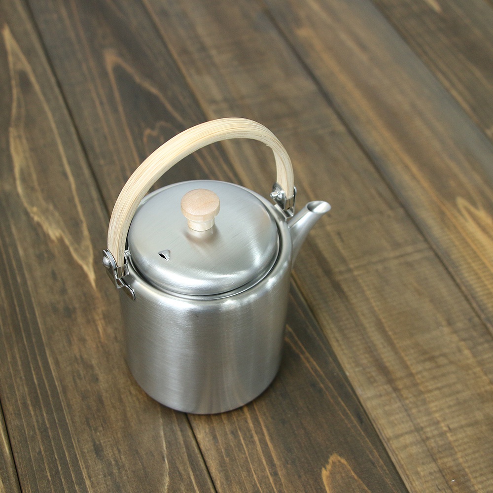 霧面不鏽鋼直筒茶壺，配有木質提把和圓形木質壺蓋旋鈕，壺身為銀色，置於深棕色木紋桌面。