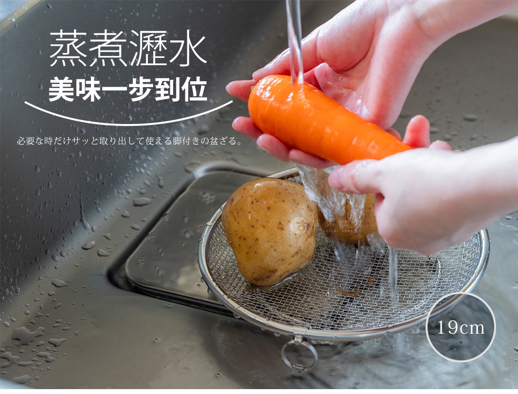 雙手正在水槽上方清洗紅蘿蔔，下方放置一個直徑19公分的圓形不鏽鋼細網瀝水盤，濾網內裝有兩顆馬鈴薯，瀝水盤邊緣附有金屬掛勾，畫面呈現出清潔食材與廚房料理的日常場景。