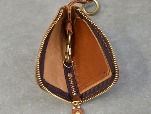職人手作皮革Organ抽繩收納鑰匙包，主體為棕色皮革，搭配黃銅色拉鍊及鑰匙圈。包內有皮革隔層，並附有可掛鑰匙的鉤扣。