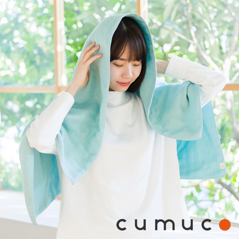 一位女性站在明亮的窗邊，頭部覆蓋著淡綠色的CUMUCO六層紗速乾浴巾，雙手輕扶布料邊緣，呈現出清新、舒適且居家自然的氛圍。