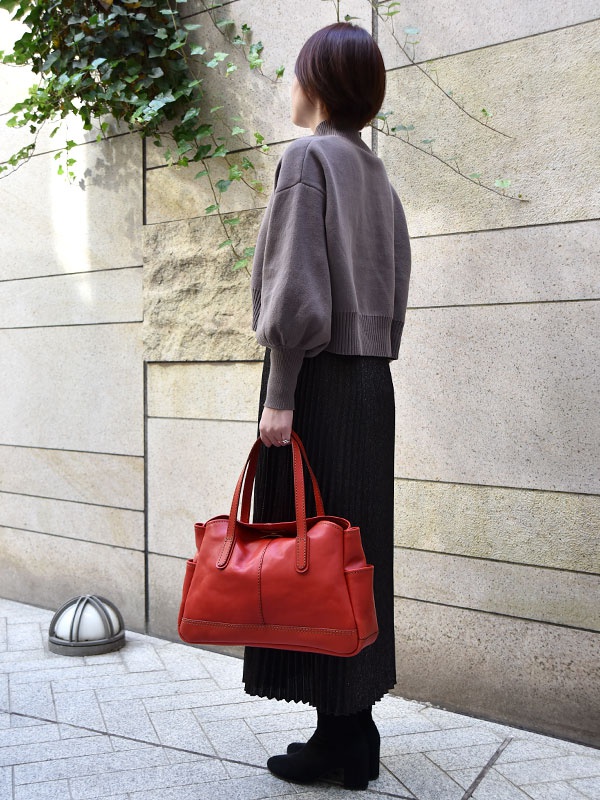 紅色皮革橫式肩背托特包，設有雙提把、正面縫線設計及兩側口袋。