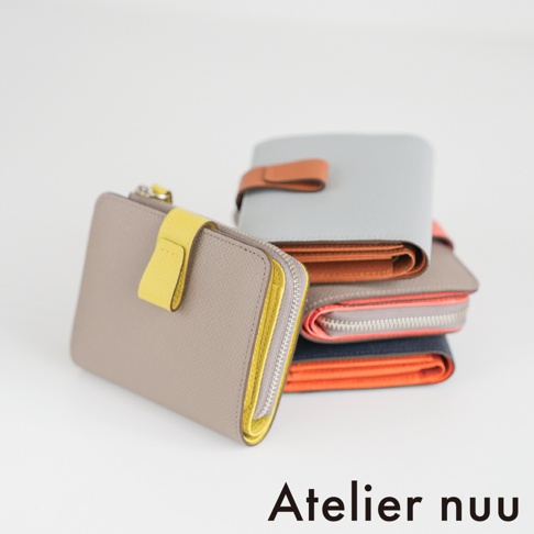 由左至右擺放多個不同配色的 Atelier nuu 皮革雙折短夾，前方為灰色搭配亮黃色飾扣的款式，後方堆疊著灰色配棕色、灰色配橘色以及深藍色配亮橘色的皮夾，展示細緻的皮革紋理與雙色設計。